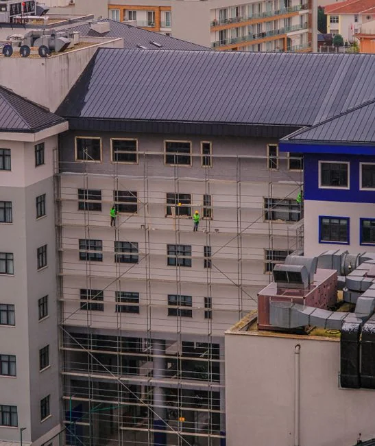 Des laveurs de vitres en hauteur, équipés de protections, nettoient la façade d’un gratte-ciel.